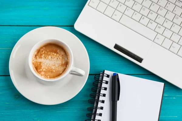 Kahve fincanı, not defteri ve ahşap turkuaz adam üstünde laptop