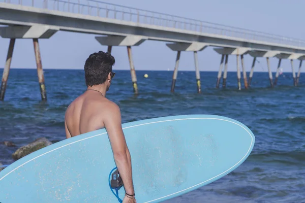 Surfista sosteniendo su tabla de surf azul por detrás —  Fotos de Stock