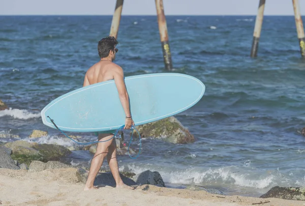 Surfer trägt sein blaues Surfbrett von hinten — Stockfoto