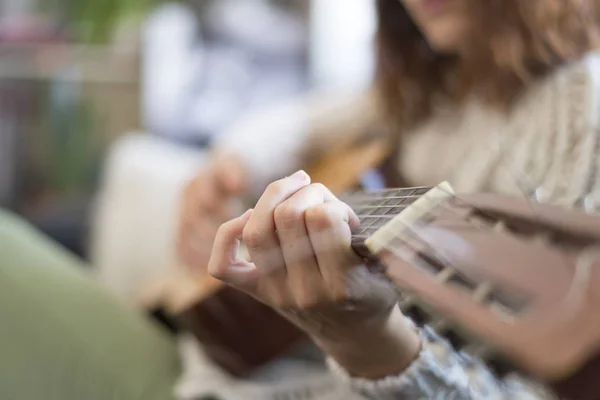 Hermosa joven sentada en el sofá tocando la guitarra — Foto de Stock