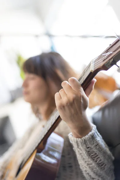 Hermosa joven sentada en el sofá tocando la guitarra — Foto de Stock