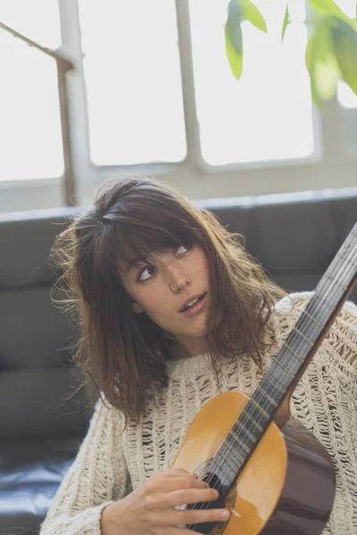 Hermosa joven sentada en el sofá tocando la guitarra — Foto de Stock