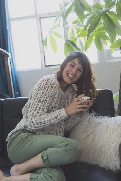 En kvinna som sitter på soffan, medan du tittar framåt och leende — Stockfoto