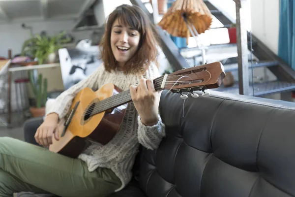 Mujer de belleza sentada en una dofa y tocando la guitarra — Foto de Stock