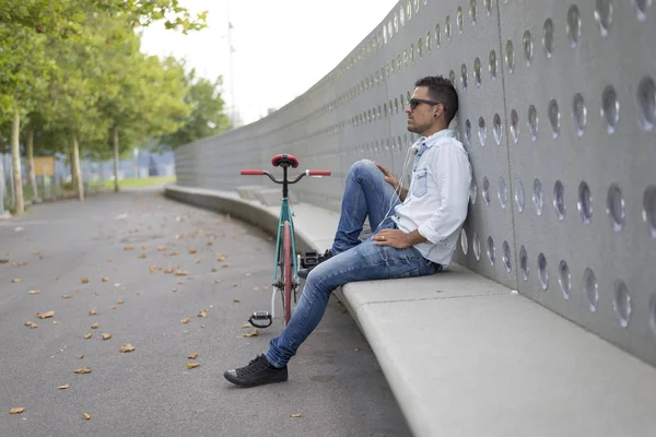 Fiatal férfi motoros pihentető egy padon, közben zenét hallgatni — Stock Fotó