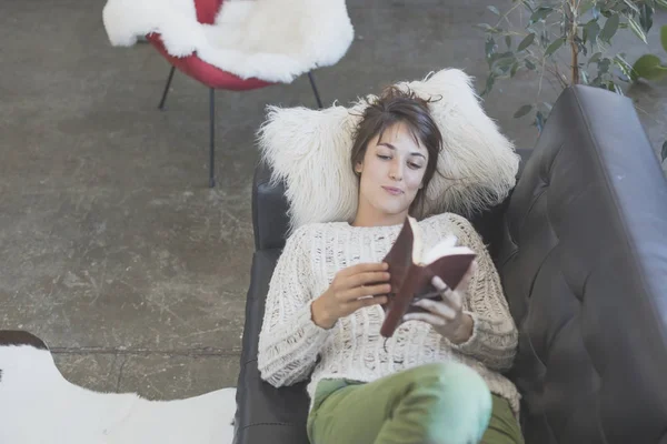 Mujer acostada en un sofá y leyendo un libro — Foto de Stock