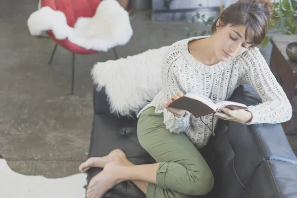 女人躺在一张沙发上，读一本书 — 图库照片