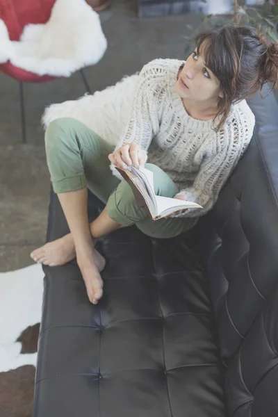 Mujer acostada en un sofá y leyendo un libro — Foto de Stock