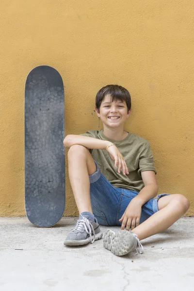 Um menino sorridente com skate sentado sozinho — Fotografia de Stock