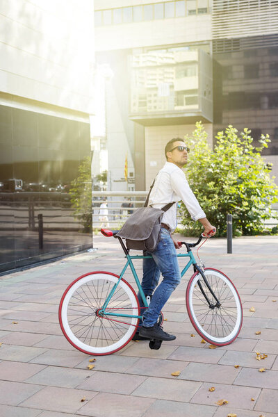 A young stylish man posing next to his bicycle.