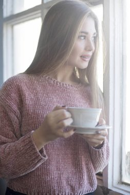 Bir fincan çay tutan pencereden bakıyor güzel kadın