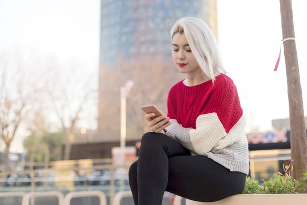 Schöne Frau schreibt eine Nachricht auf ihr Handy, während sie auf sitzt — Stockfoto