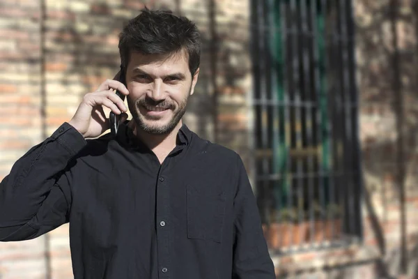 Joven hombre de negocios urbano en el teléfono inteligente en la calle hablando en smar — Foto de Stock