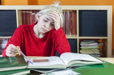 yorgun öğrenci başını çok kitap ele oturuyor.