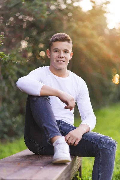 Stylish teenager sitting on a wooden bench on a city park — Stock Photo, Image