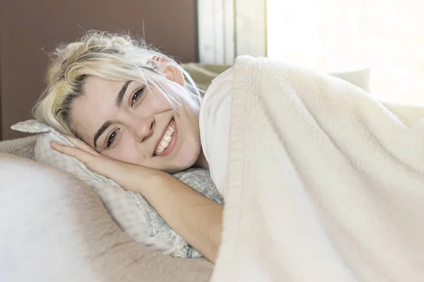 Una hermosa mujer feliz contenido acostada en la cama sonriendo a la cámara . — Foto de Stock