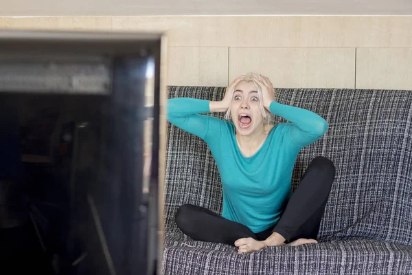 beautiful young surprised woman watching TV at home alone.