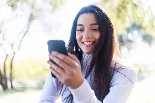 Retrato de una joven hispana usando teléfono móvil en el parque el día soleado sonriendo - mujer muy feliz en el teléfono celular — Foto de Stock