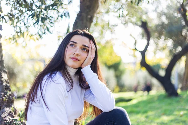 Mladá zamyšlená žena sedí v parku a dívá se jinam — Stock fotografie