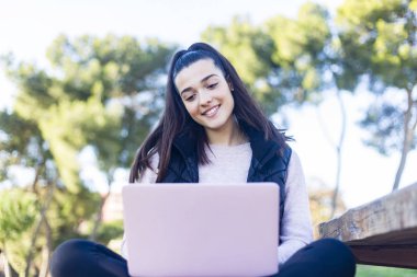 Young beautiful woman sitting outdoors while working with laptop clipart