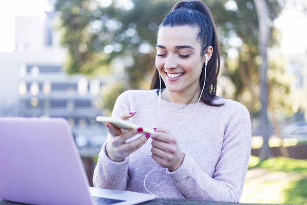 Mujer joven de 20 años en ropa casual relajante en el parque verde, y el uso de teléfono móvil con auriculares — Foto de Stock