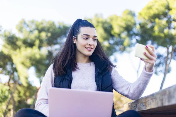 Young beautiful woman with ponytail using a smartphone outdoors to make a video conference