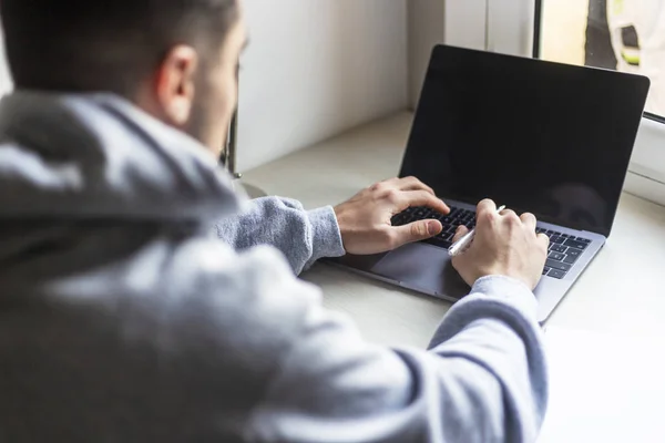 Achteraanzicht van een jongeman die thuis met laptop op het bureaublad werkt — Stockfoto