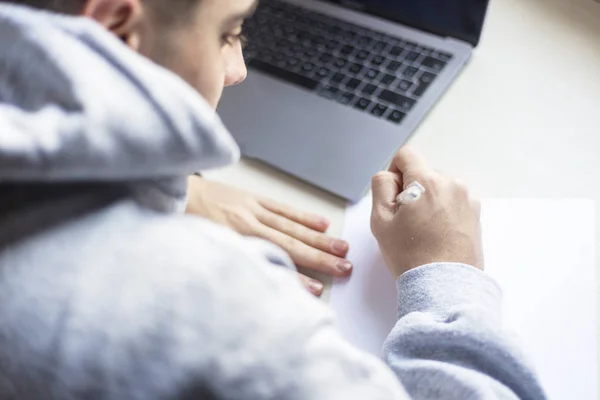 Achteraanzicht van een jongeman die thuis op papier schrijft naast een laptop — Stockfoto