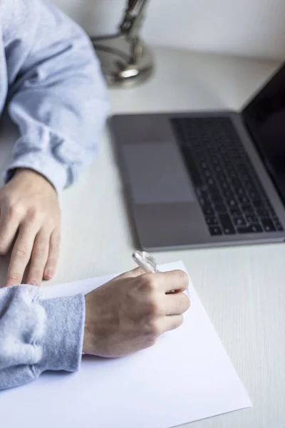 Achteraanzicht van een jongeman die thuis op papier schrijft naast een laptop — Stockfoto