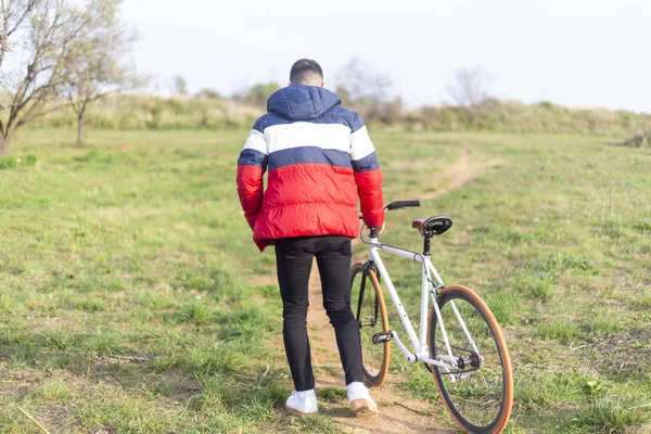 Achteraanzicht van een jongeman die met een vaste fiets over een park loopt — Stockfoto