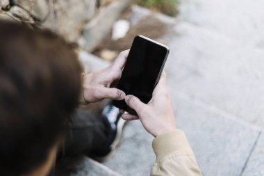 Dışarda otururken cep telefonu kullanan İspanyol bir gencin arka görüntüsü.