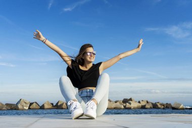 Uzun saçlı güzel bir kadın mavi gökyüzüne karşı gezinirken büyük bir gülümsemeyle yüzünü çeviriyor.