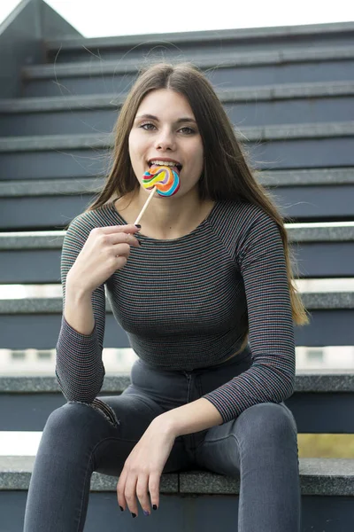 Attractive young woman with lollipop sitting on steps outside