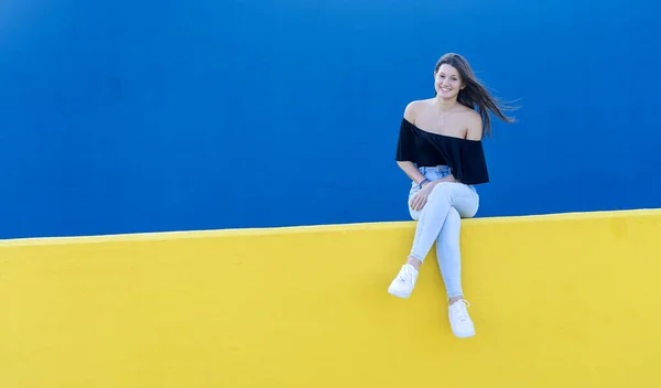 Νεαρή Όμορφη Γυναίκα Μακριά Μαλλιά Κάθεται Κίτρινο Τοίχο Ενώ Αναζητούν — Φωτογραφία Αρχείου