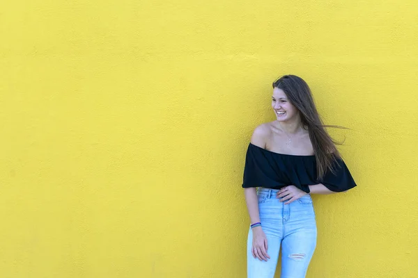 Beautiful girl leaning on yellow wall, young friendly woman smiling happy outdoors a day of summer