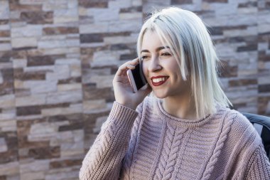 Terasta kanepede oturan genç ve güzel bir kadın cep telefonuyla konuşuyor.