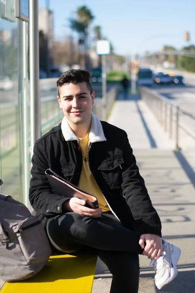 Mladý Student Sedí Zkříženýma Nohama Autobusové Zastávce Úsměvem Dívá Kamery — Stock fotografie