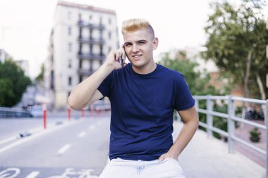 Sokakta cep telefonu kullanan genç sarışın bir erkek.