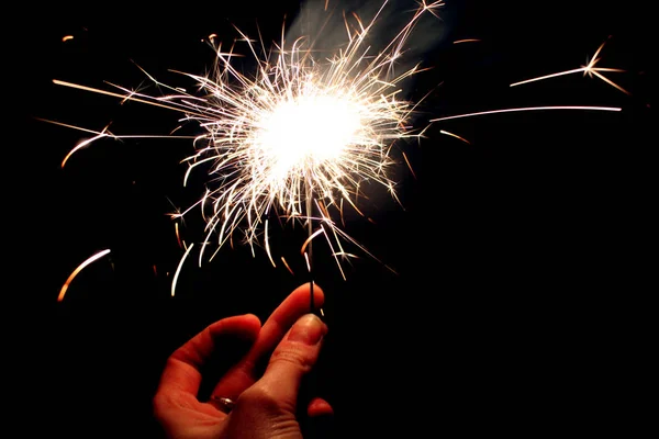 Womans hand holding burning Sparkler in hand in the dark on black background. Celebration concept