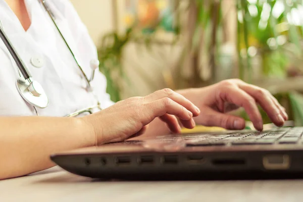 Beyaz üniformalı ve steteskoplu bir kadın doktor ev ofisinden bilgisayarı yakın çekimde çalışıyor. Teletıp, tıbbi danışmanlık, tele sağlık, 911, uzaktan sağlık konsepti.