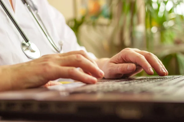Beyaz üniformalı ve steteskoplu bir kadın doktor ev ofisinden bilgisayarı yakın çekimde çalışıyor. Teletıp, tıbbi danışmanlık, tele sağlık, 911, uzaktan sağlık konsepti.