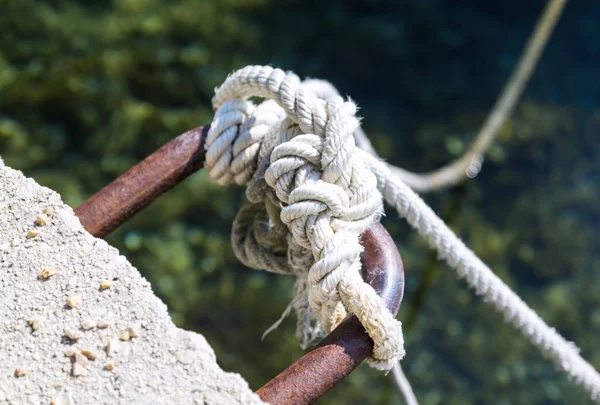 Mooring bollard, knot rope and sea background
