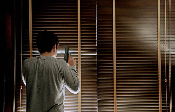 Silahlı bir adam pencerenin yanında kör bir şekilde duruyor, kendisini başka kötü insanlardan korumaya hazır, suç mahalli kavramsal.     