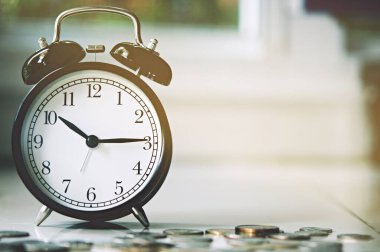 Bulanık klasik çalar saat, seçici odak ve sığ alan derinliği ve yatırım konseptiyle yere yerleştirilmiş büyüyen bozuk paralar. Para, İş Finansmanı ve Tasarruf.