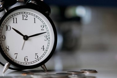 Bulanık klasik çalar saat, seçici odak ve sığ alan derinliği ve yatırım konseptiyle yere yerleştirilmiş büyüyen bozuk paralar. Para, İş Finansmanı ve Tasarruf.