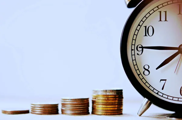 Bulanık klasik çalar saat, seçici odak ve sığ alan derinliği ve yatırım konseptiyle yere yerleştirilmiş büyüyen bozuk paralar. Para, İş Finansmanı ve Tasarruf.