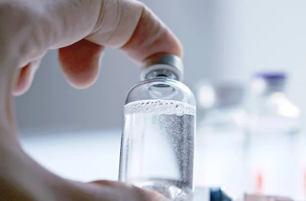 Glass medical bottle in a doctor\'s hand. A bottle with a vaccine holds a hand in a hospital. Technician prepares the vaccine. Preventing the spread of viruses through vaccination.