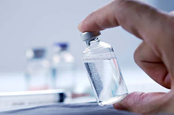 Glass medical bottle in a doctor\'s hand. A bottle with a vaccine holds a hand in a hospital. Technician prepares the vaccine. Preventing the spread of viruses through vaccination.