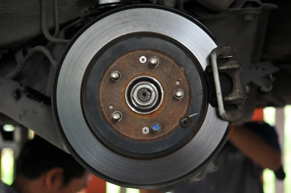 Auto mechanic in process of new tire replacement, Car brake repairing in garage, Brakes on a car with removed wheel, car brake part at garage,car brake disc without wheels closeup