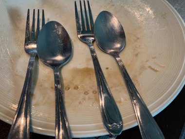 Restoranda yemek yedikten sonra tahta masada çatal ve kaşıkla boş ve kirli bir tabak. Karışıklık konsepti, kirli bulaşıklar. Sağlığa zararlı..